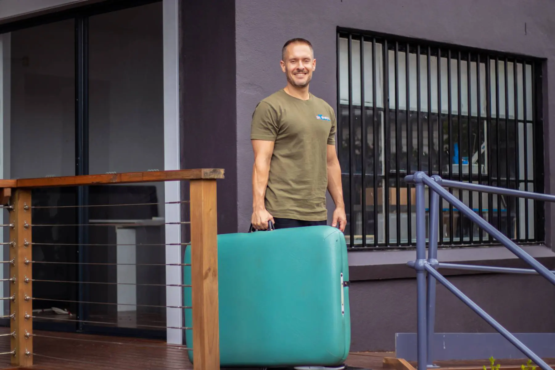 Alex Bastianon smiling and holding a portable massage table about to visit a client who requested he goes to their house