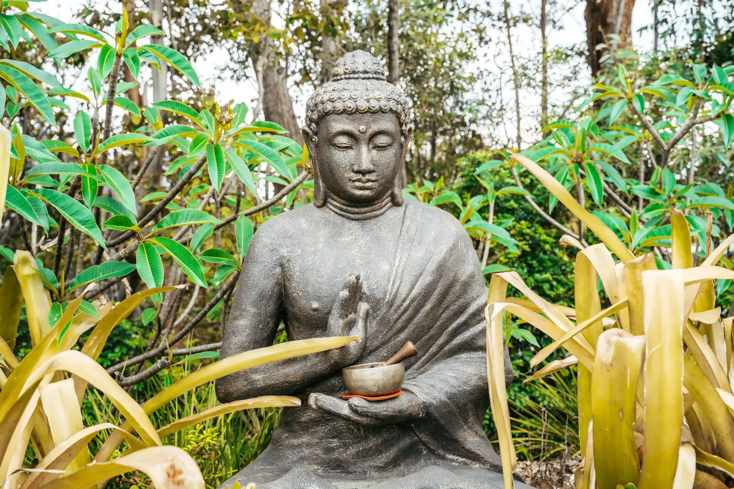 A Large stone buddha in meditation holding a Tibetan sound bowl in the palm of his hand