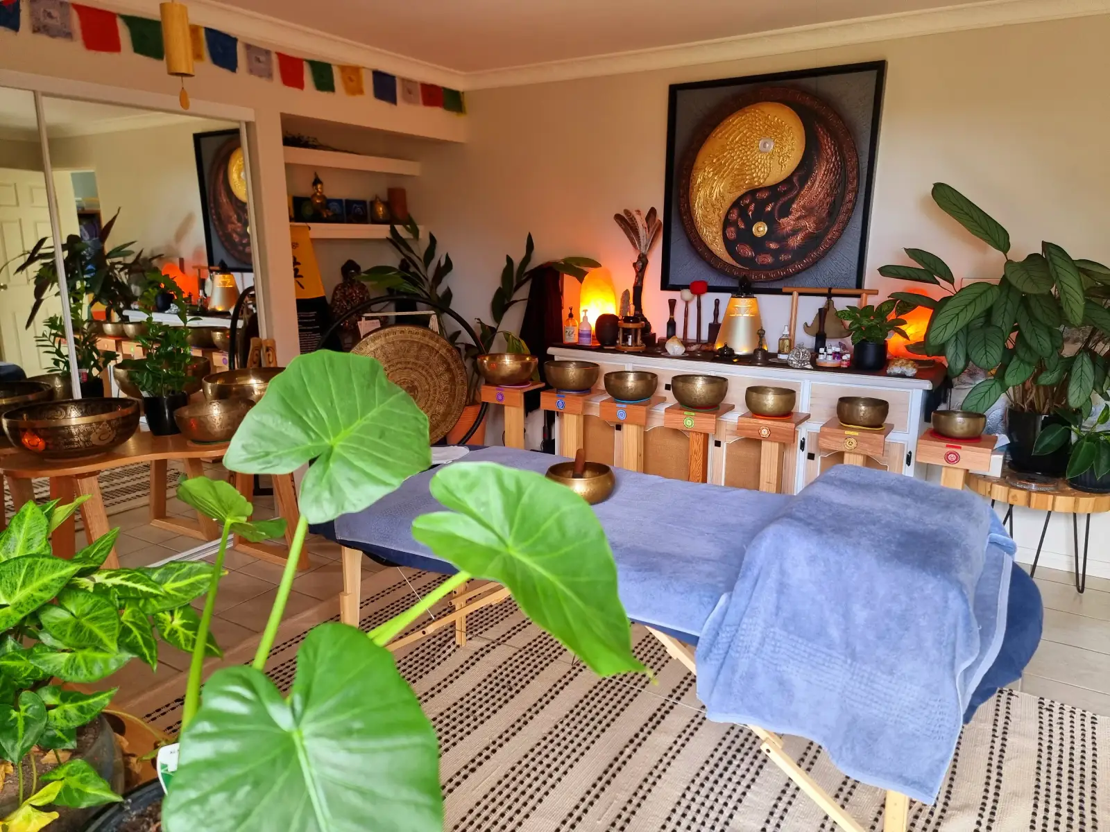 Alex Bastianon's massage room with seven singing bowls, massage table, indoor plants and a painting of a yin-yang symbol