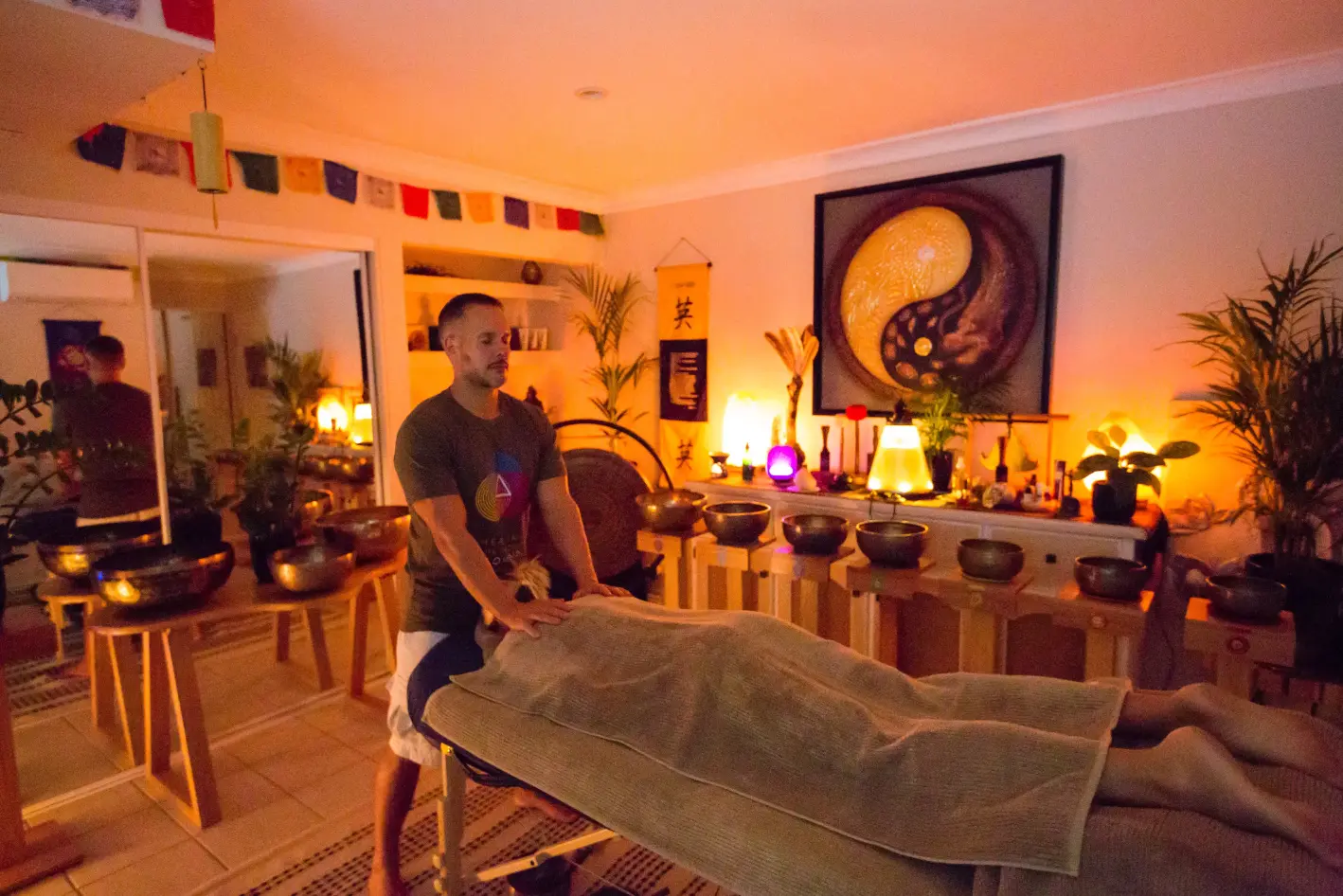 Alex Bastianon doing remedial massage on a woman laying facedown on a massage table with sound bowls in the background