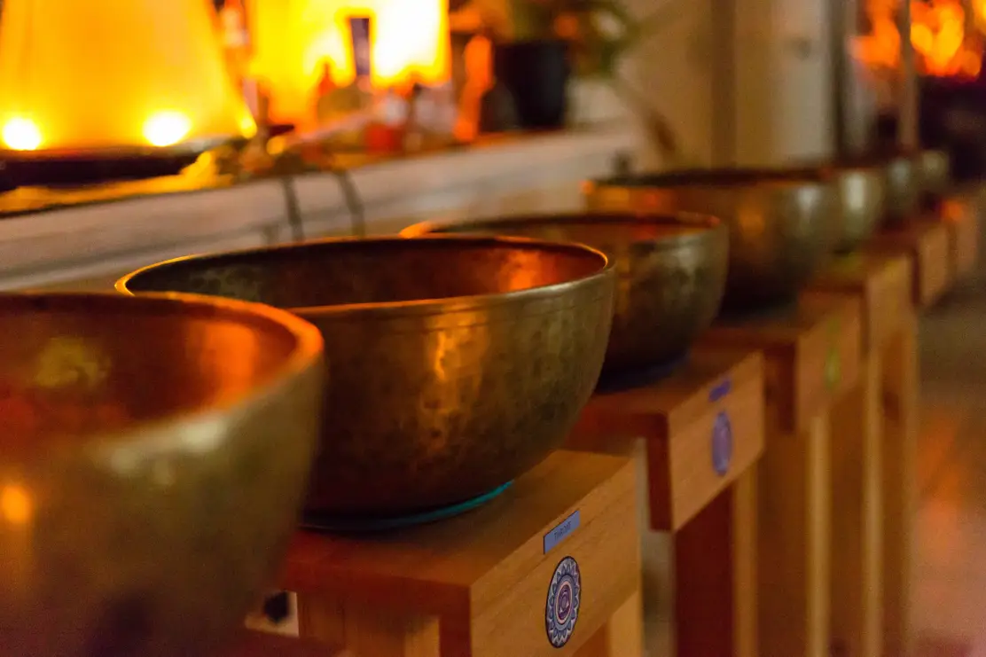 A bunch of metal Tibetal singing bowls sitting on wooden tables with orange lighting