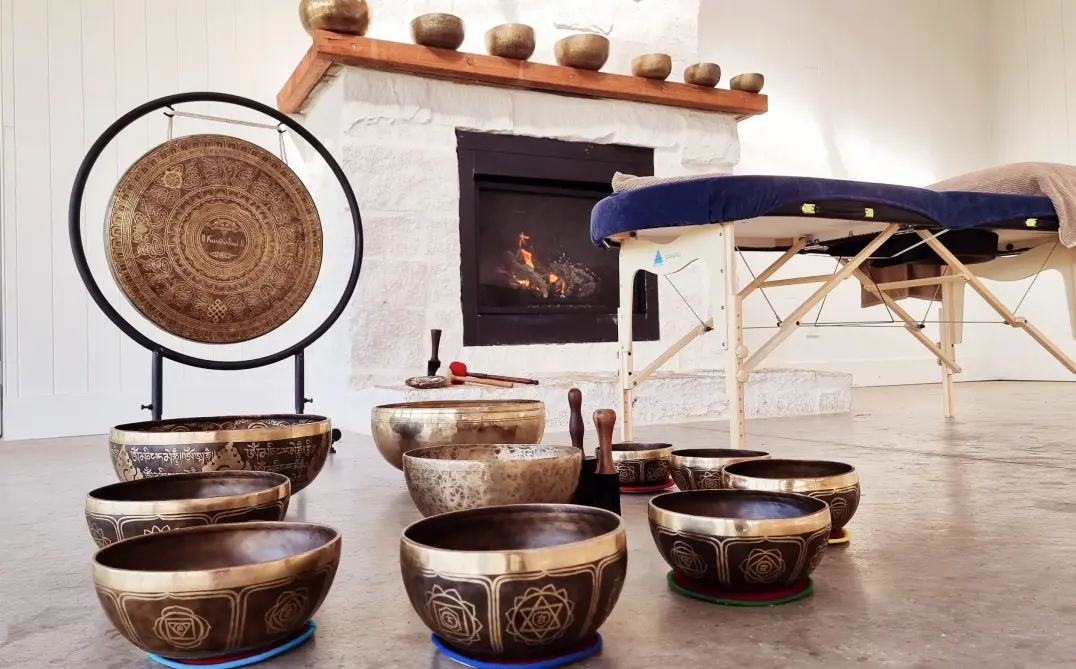 Large, medium and small Tibetan sound bowls and sound healing gong in a room with a fireplace and massage table