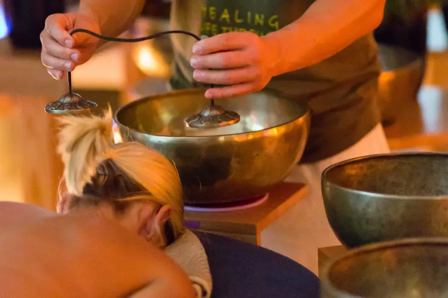 A woman laying facedown on a massage table with Alex Bastianon doing a sound healing