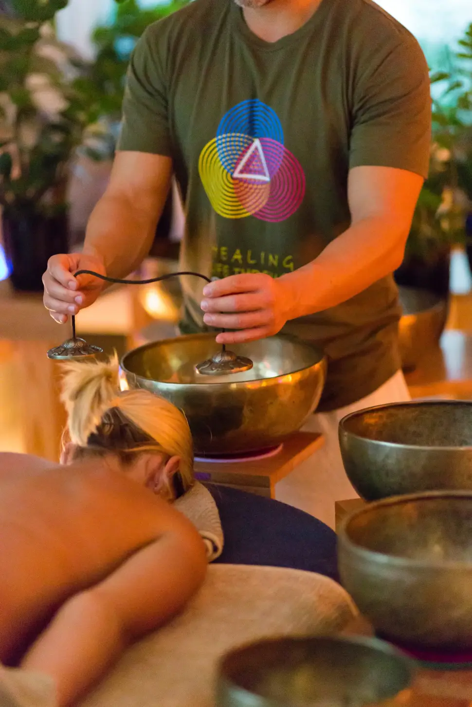 Alex Bastianon doing sound healing on a blonde woman laying facedown on a massage table