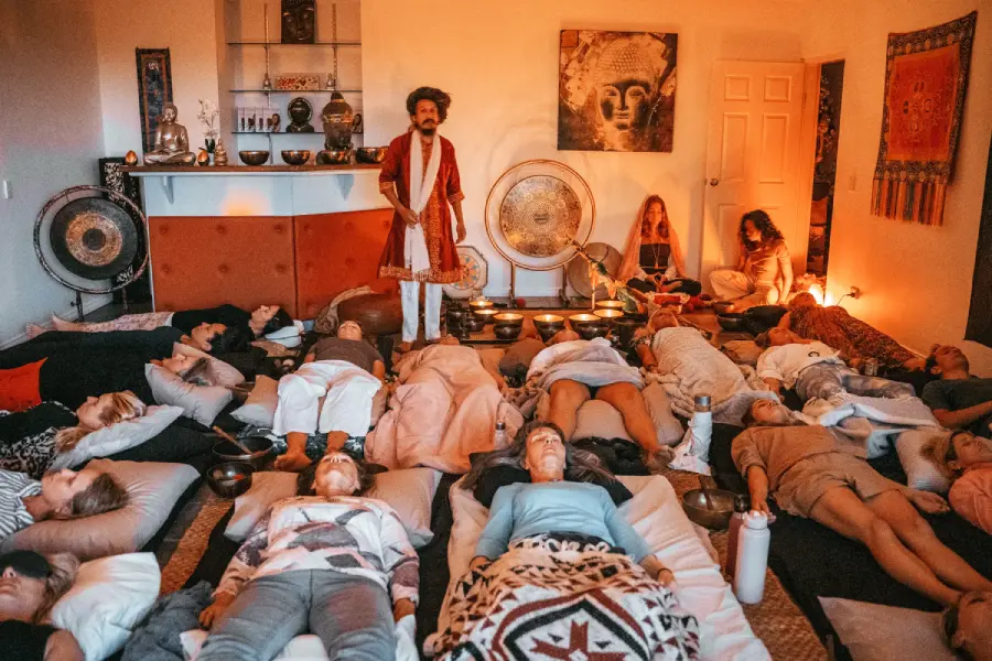 A group of people laying on the floor with Master Chaitanyashree doing sound healing using singing bowl and large gongs